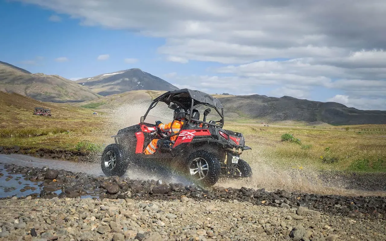 Rauður buggybíll á fullri ferð eftir malarslóða með fjöll í baksýn